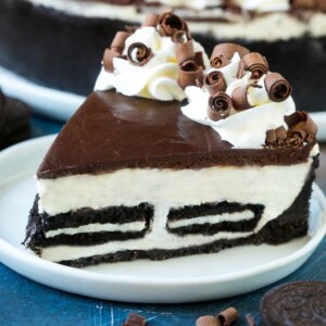 A slice of no bake Oreo cheesecake with a cookie crust, cheesecake and Oreo filling and chocolate topping.