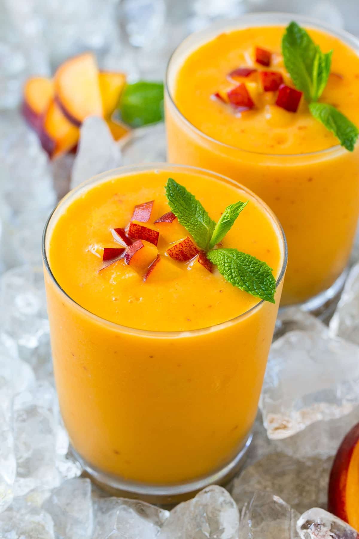 A glass of peach smoothie topped with chopped peaches and fresh mint.