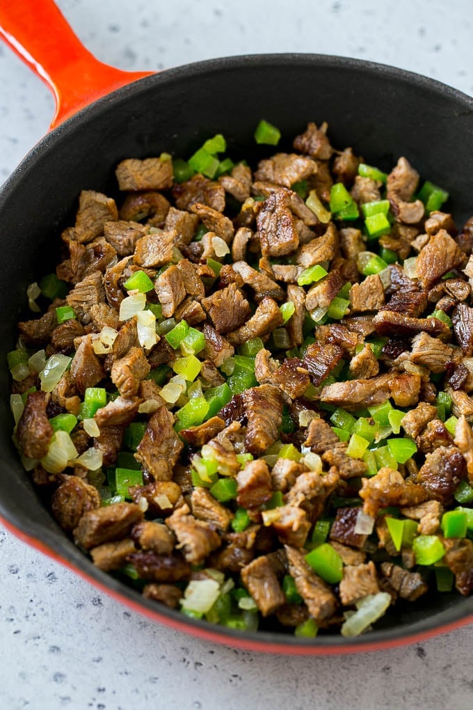 Seared rib eye steak, peppers and onions in a pan.