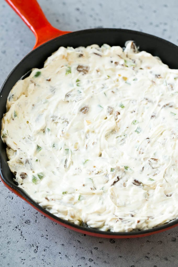 Steak, peppers and onions in a skillet, mixed with cream cheese.