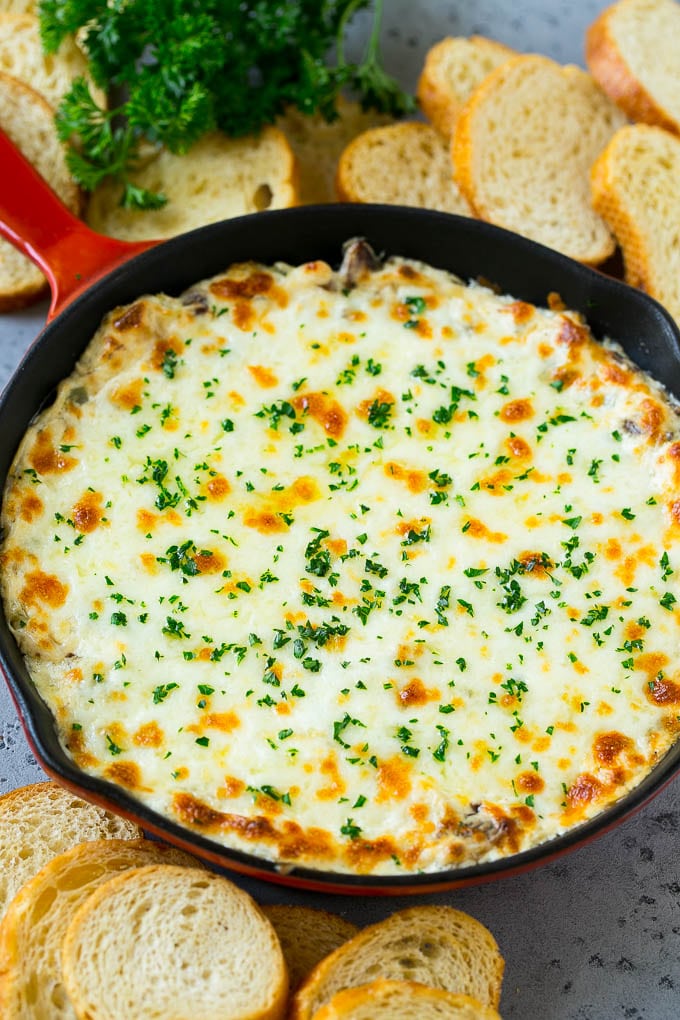 A skillet of baked Philly cheesesteak dip with melted cheese and parsley on top.