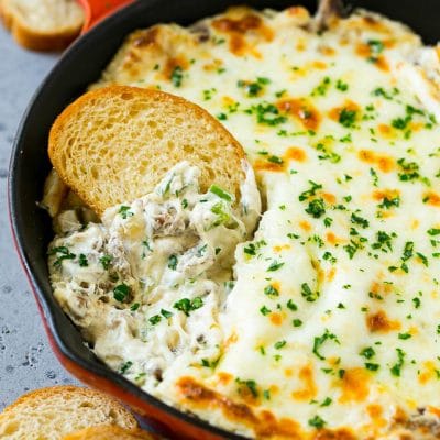 Philly cheesesteak dip with a baguette piece scooping some dip out.