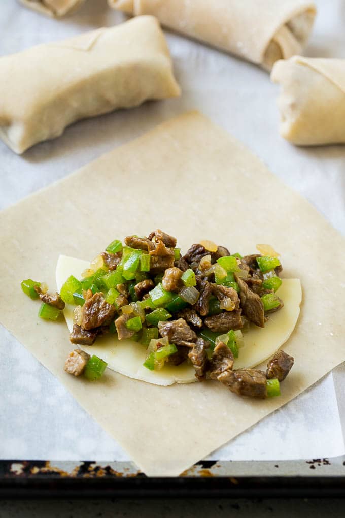 An egg roll wrapper topped with a slice of provolone cheese, steak and peppers.