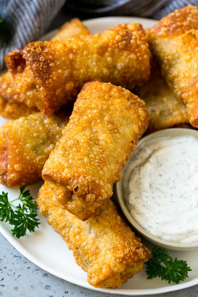 A plate of Philly cheesesteak egg rolls with a side of ranch for dipping.