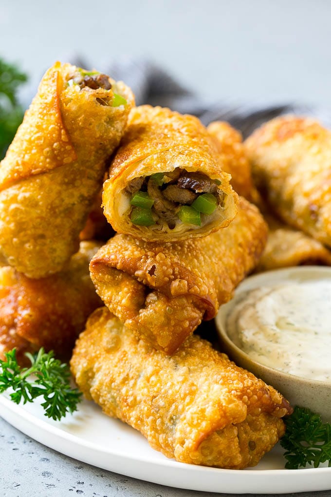 A serving plate of Philly cheesesteak egg rolls filled with rib eye steak, peppers and onions.