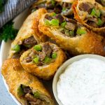 A plate of Philly cheesesteak egg rolls filled with diced steak, peppers, onions and cheese.