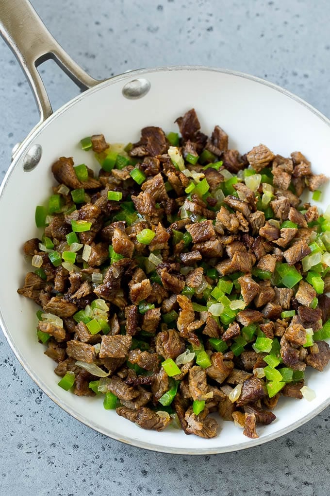 A pan of sauteed rib eye steak, peppers and onions.