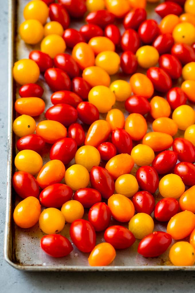 Red, orange and yellow cherry tomatoes on a sheet pan.