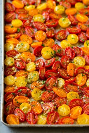 Roasted cherry tomatoes with garlic, olive oil and herbs on a sheet pan.