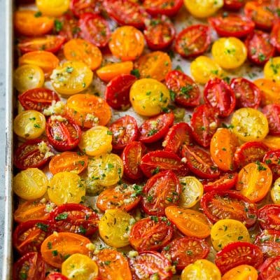 Roasted cherry tomatoes with garlic, olive oil and herbs on a sheet pan.