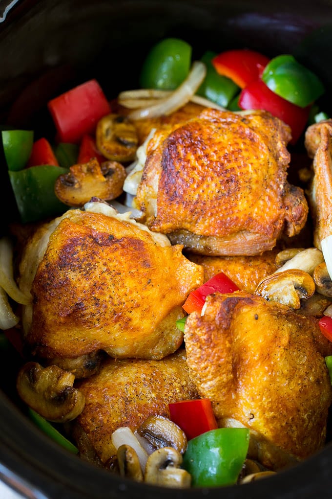 Chicken thighs with peppers, onions and mushrooms inside a slow cooker.