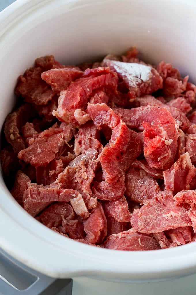 Flank steak strips tossed in cornstarch inside a slow cooker.