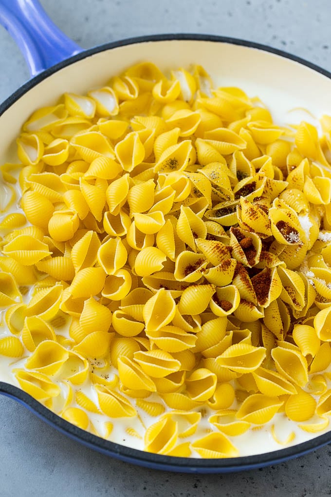 Shell pasta and spices in milk in a skillet.