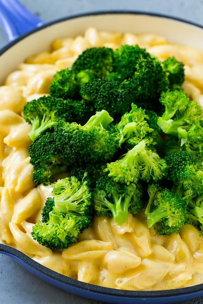 Mac and cheese in a skillet with steamed broccoli florets.