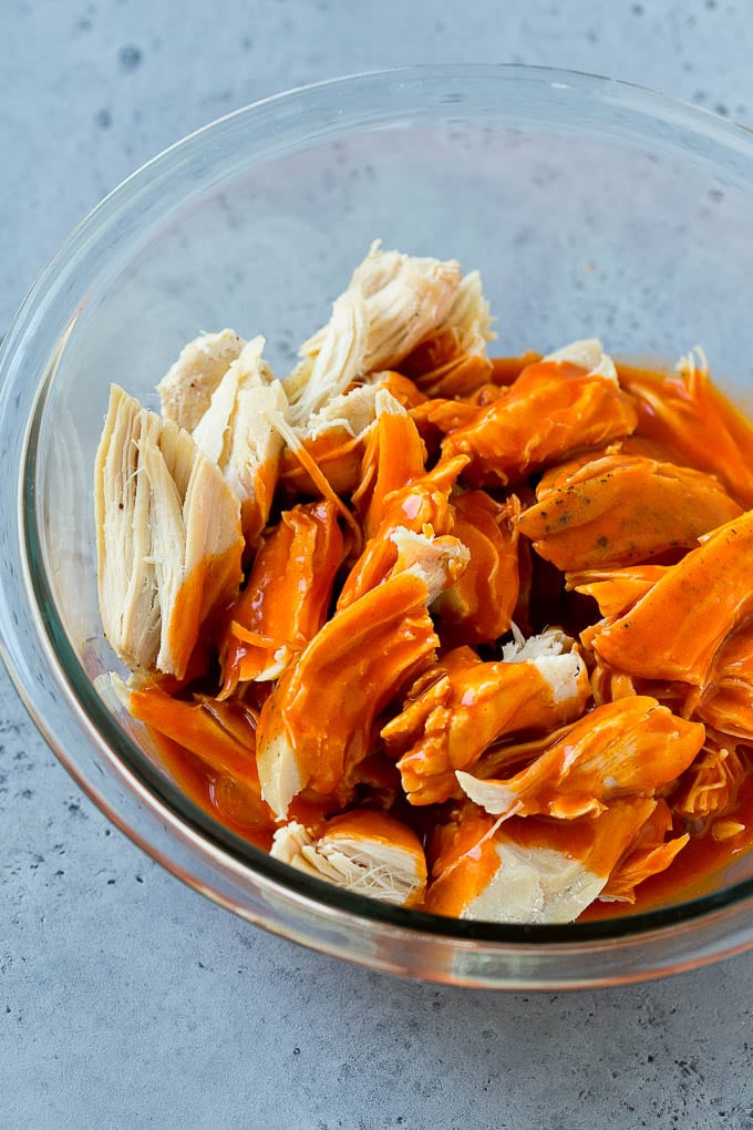 Shredded chicken in a bowl drizzled with buffalo sauce.