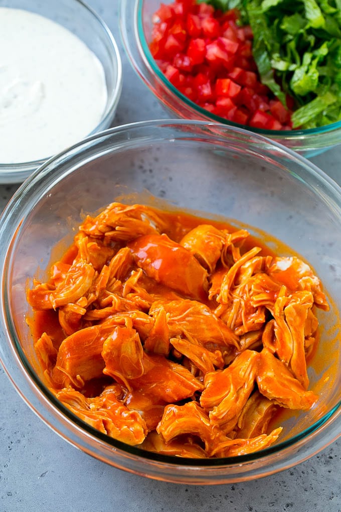 Chicken tossed with buffalo sauce along with bowls of ranch, tomatoes and lettuce.