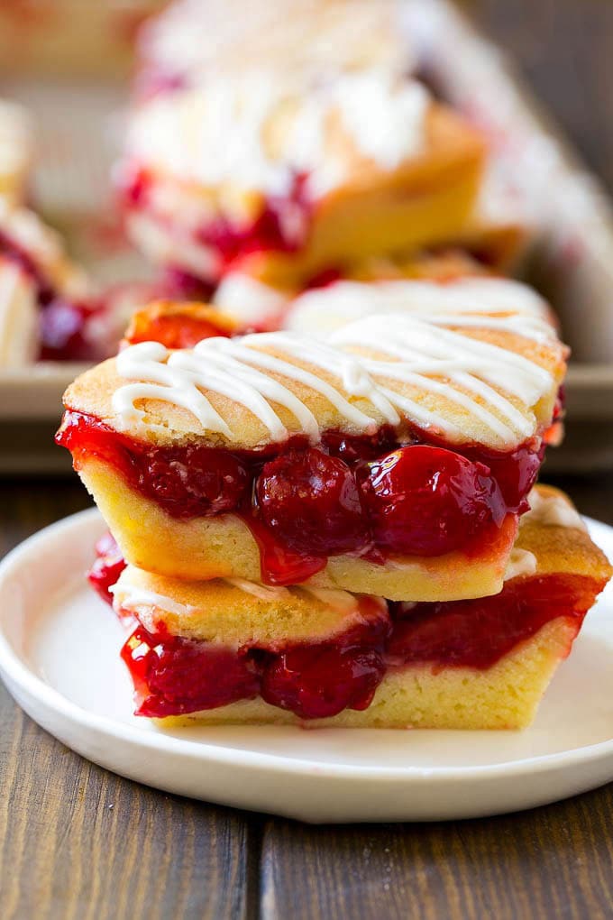 Two cherry bars on a plate with a pan of bars in the background.