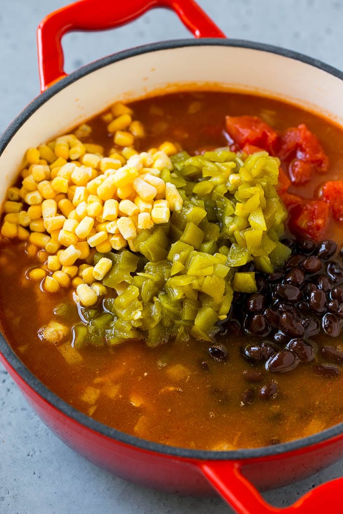 A soup pot full of shredded chicken, tomatoes, chiles, black beans, corn and broth.