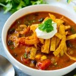 A bowl of chicken enchilada soup topped with tortilla strips, sour cream and cilantro.