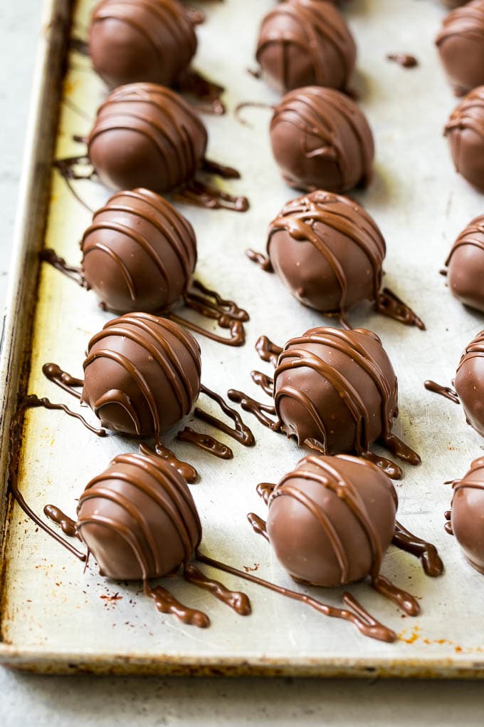 Chocolate covered cherries on a sheet pan with a chocolate drizzle on top.