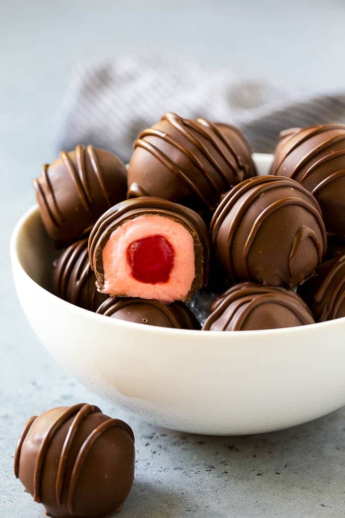 A bowl of chocolate covered cherries with one cut open.