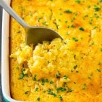 A pan of corn pudding with a serving spoon in it.
