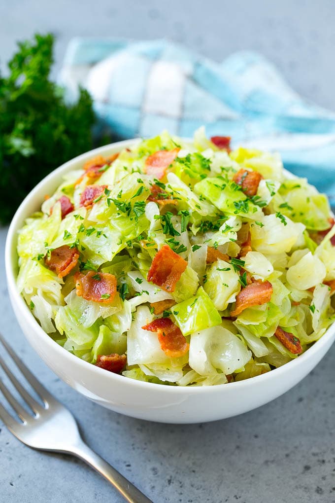 A bowl of fried cabbage topped with bacon and parsley.