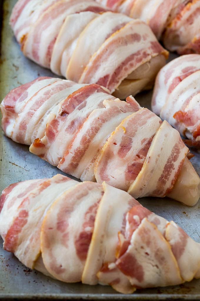 Chicken wrapped in slices of raw bacon to be baked in the oven.