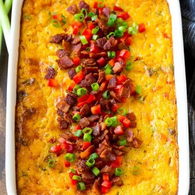 A casserole of loaded corn casserole topped with bacon, red peppers and green onions.