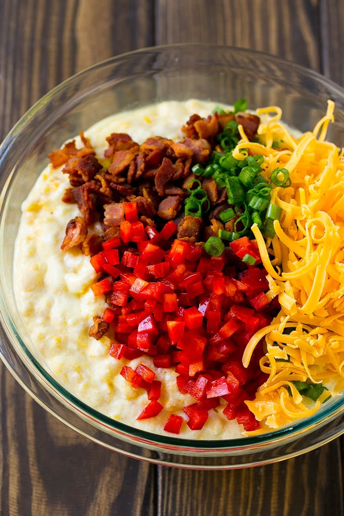 A bowl of batter with red pepper, green onions, cheddar cheese and bacon.