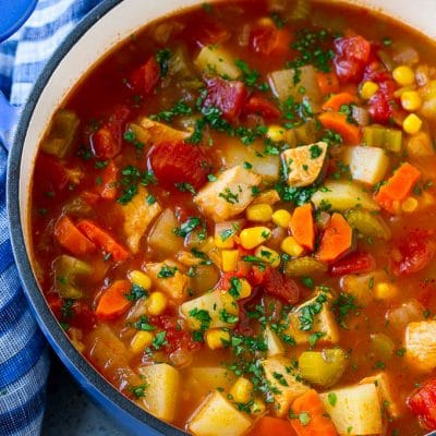 A pot of Mexican chicken soup with colorful veggies and potatoes, all topped with cilantro.
