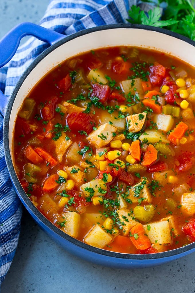 A pot of Mexican chicken soup with colorful veggies and potatoes, all topped with cilantro.