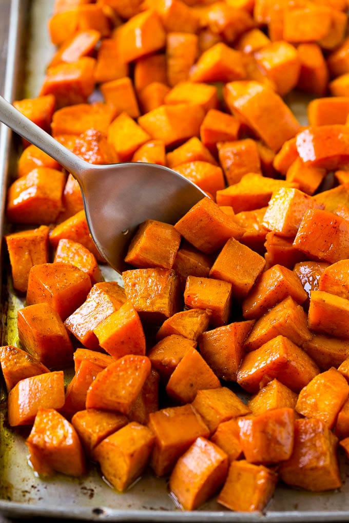 A sheet pan of baked yams flavored with maple and cinnamon, with a serving spoon in them.