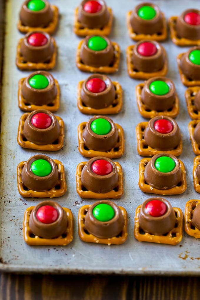 Rolo pretzels with red and green M&M's on a baking sheet.