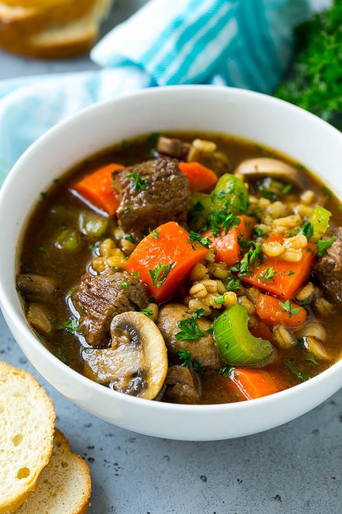 A bowl of beef barley soup topped with chopped parsley.