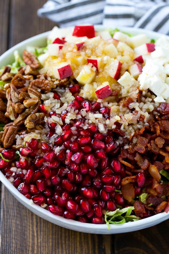 Dressing poured on top of salad that contains sprouts, pomegranate seeds, pecans and bacon.