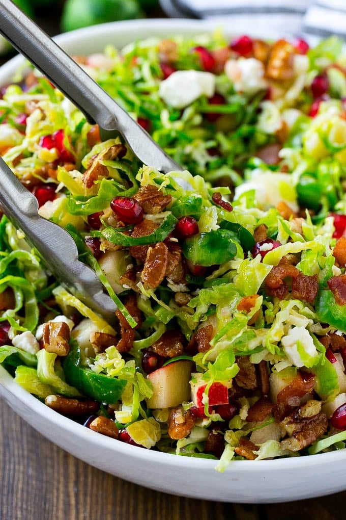 A bowl of brussels sprout salad with tongs picking some up out of the bowl.