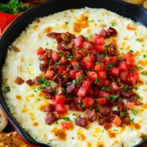 Baked chicken Alfredo dip in a skillet topped with bacon, tomatoes and chopped parsley.