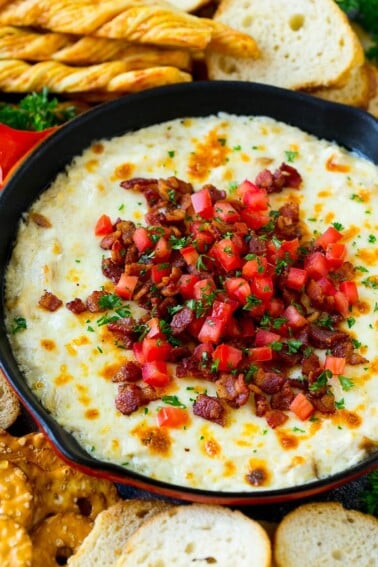 Baked chicken Alfredo dip in a skillet topped with bacon, tomatoes and chopped parsley.