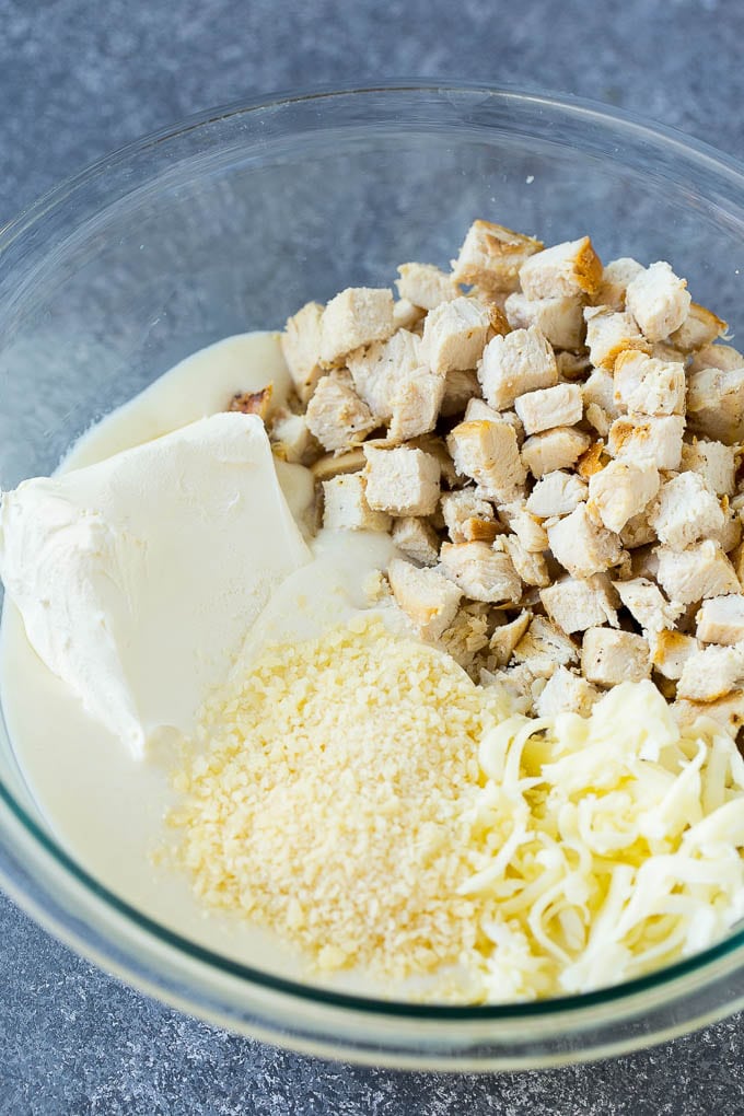 Chicken, Alfredo sauce, cream cheese, mozzarella and parmesan cheese in a mixing bowl.