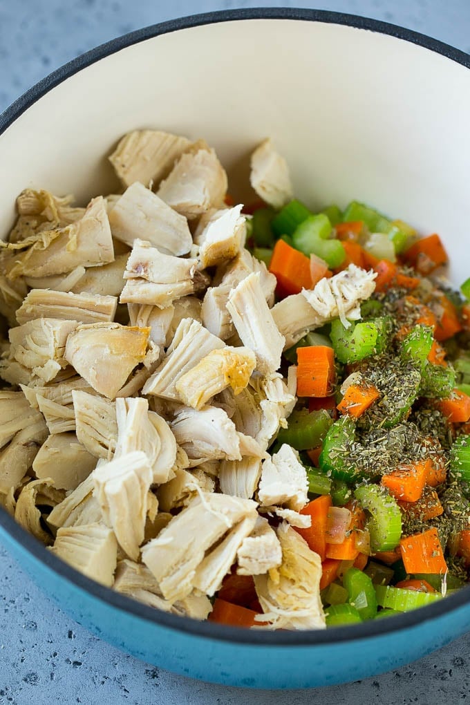 Vegetables, shredded chicken and dried herbs in a soup pot.