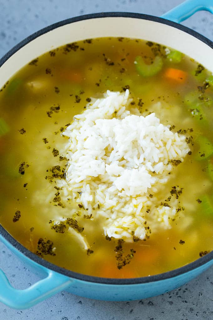 Chicken soup with rice being stirred into it.