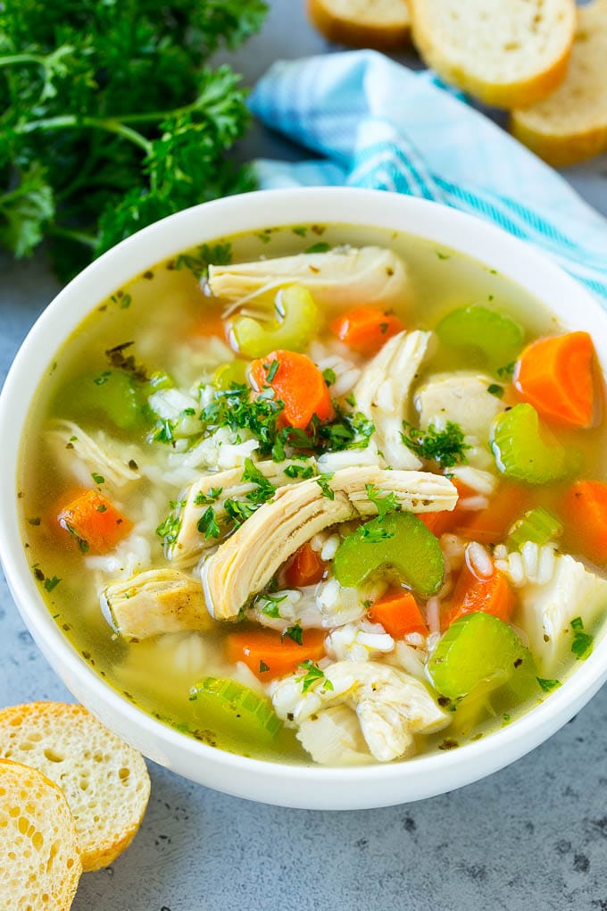A bowl of chicken and rice soup with vegetables, garnished with chopped parsley leaves.