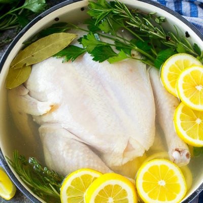 Chicken brine in a pot with a whole chicken, lemons, herbs and spices.