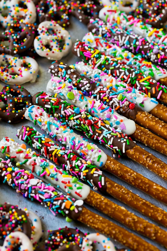 A sheet pan with chocolate covered pretzel twists and rods decorated with rainbow sprinkles.