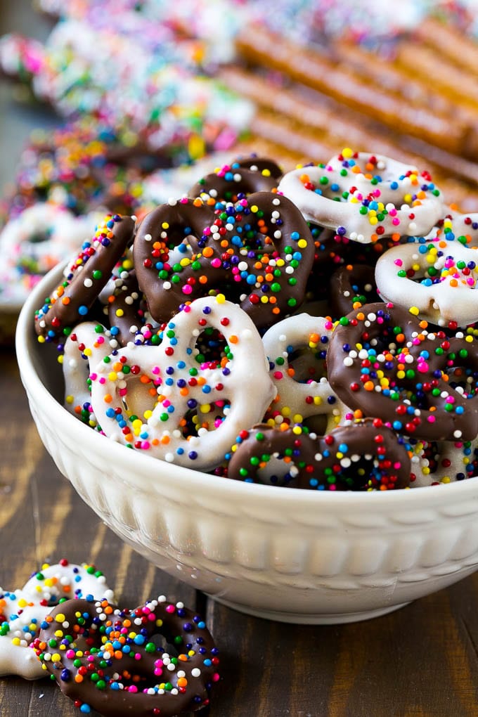 A bowl of chocolate covered pretzels decorated with rainbow sprinkles.