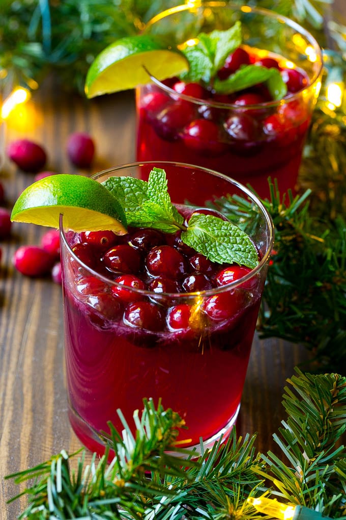 Glasses of Christmas punch garnished with fresh cranberries, mint sprigs and lime wedges.