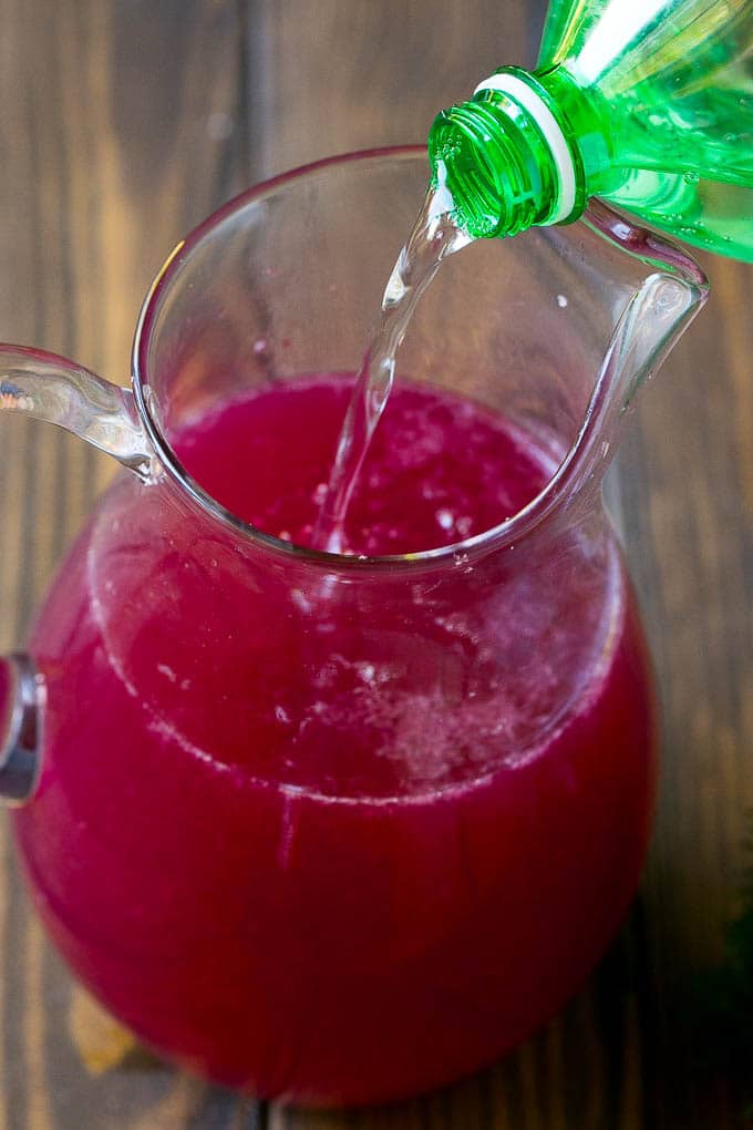 Sparkling water being poured into a pitcher of pomegranate and cranberry juice.