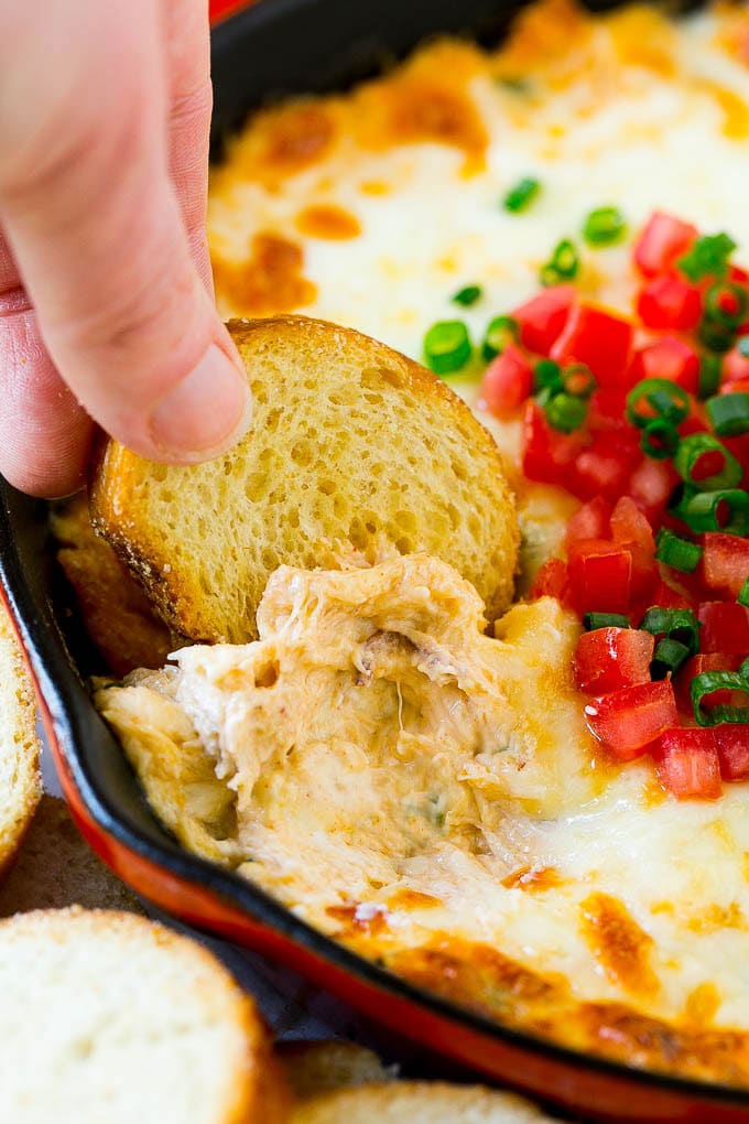 A hand scooping out some crap dip with a crostini toast.