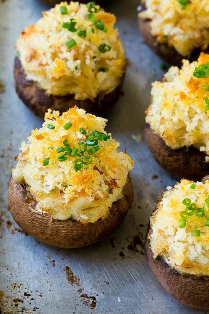 Crab stuffed mushrooms on a sheet pan topped with sliced chives.